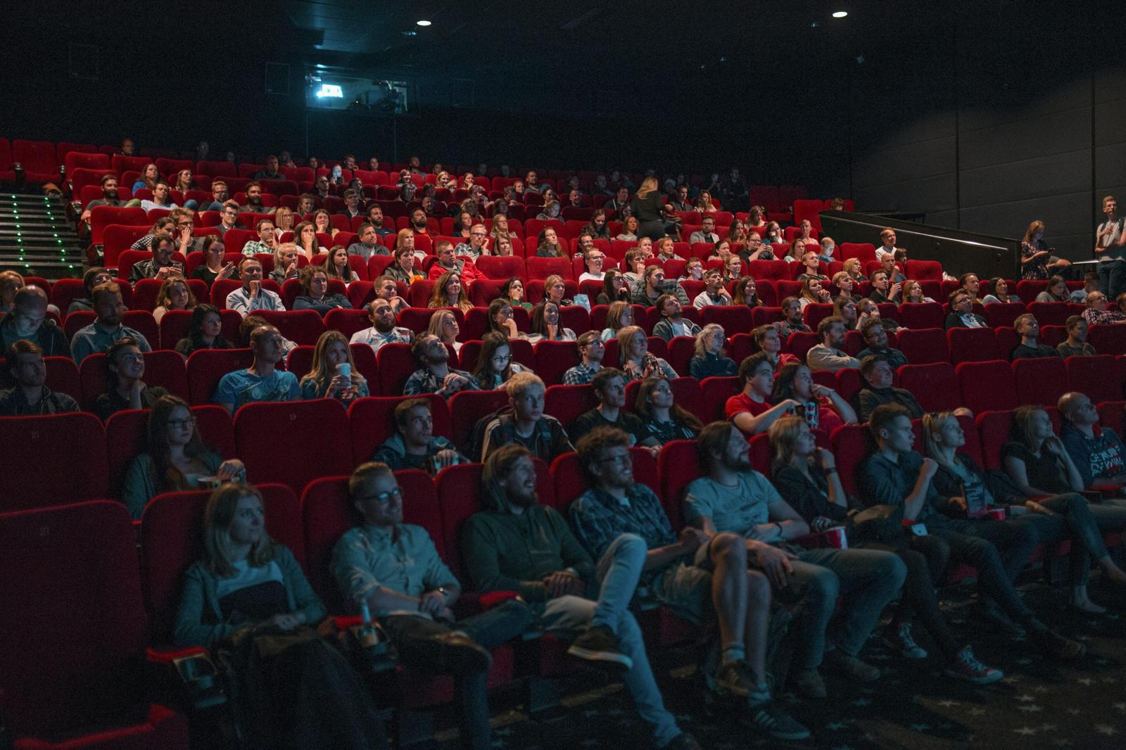 An audience seated in rows of red seats in a darkened auditorium.
